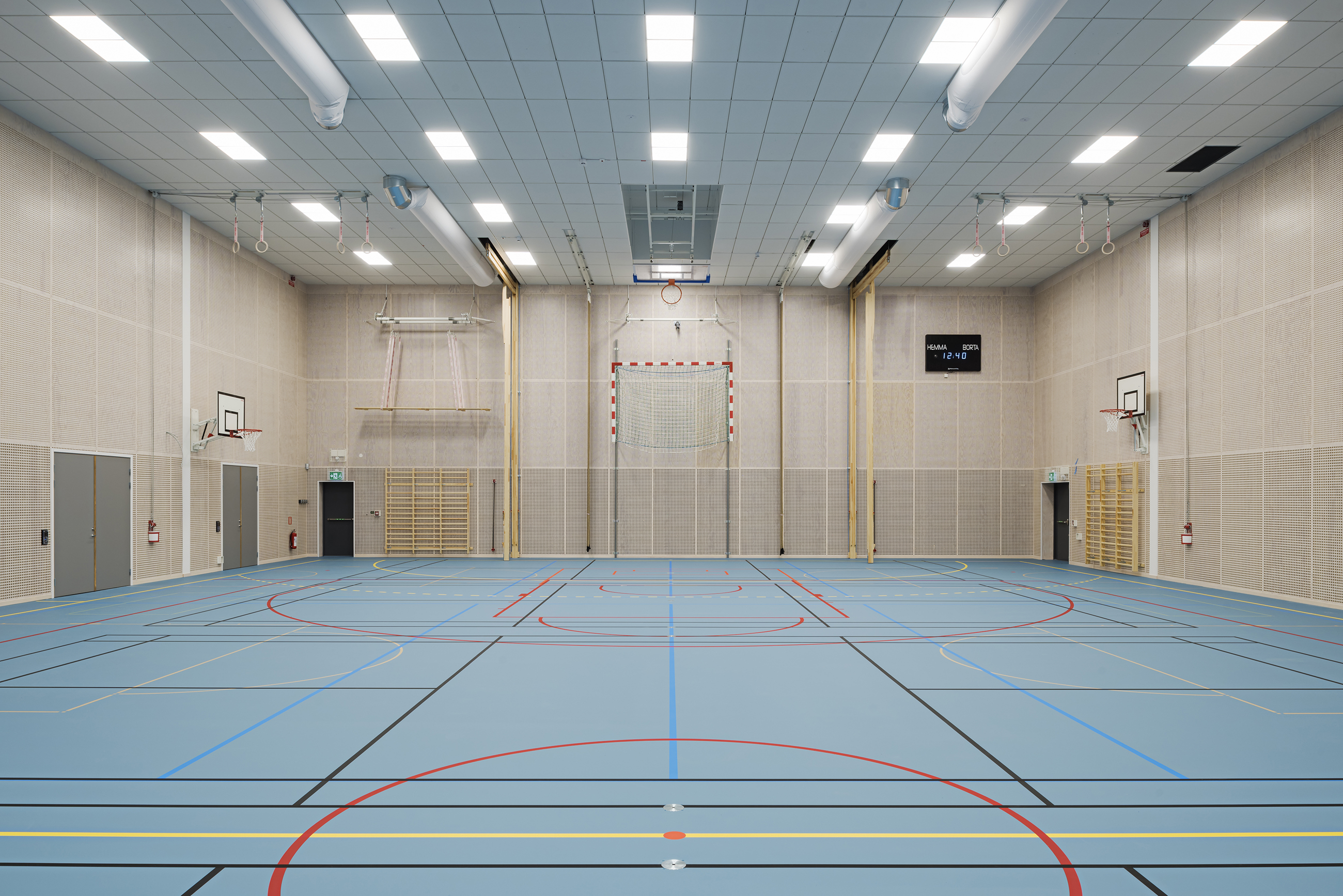 Gymnastiksal med perforerede paneler på væggene og blåt gulv
