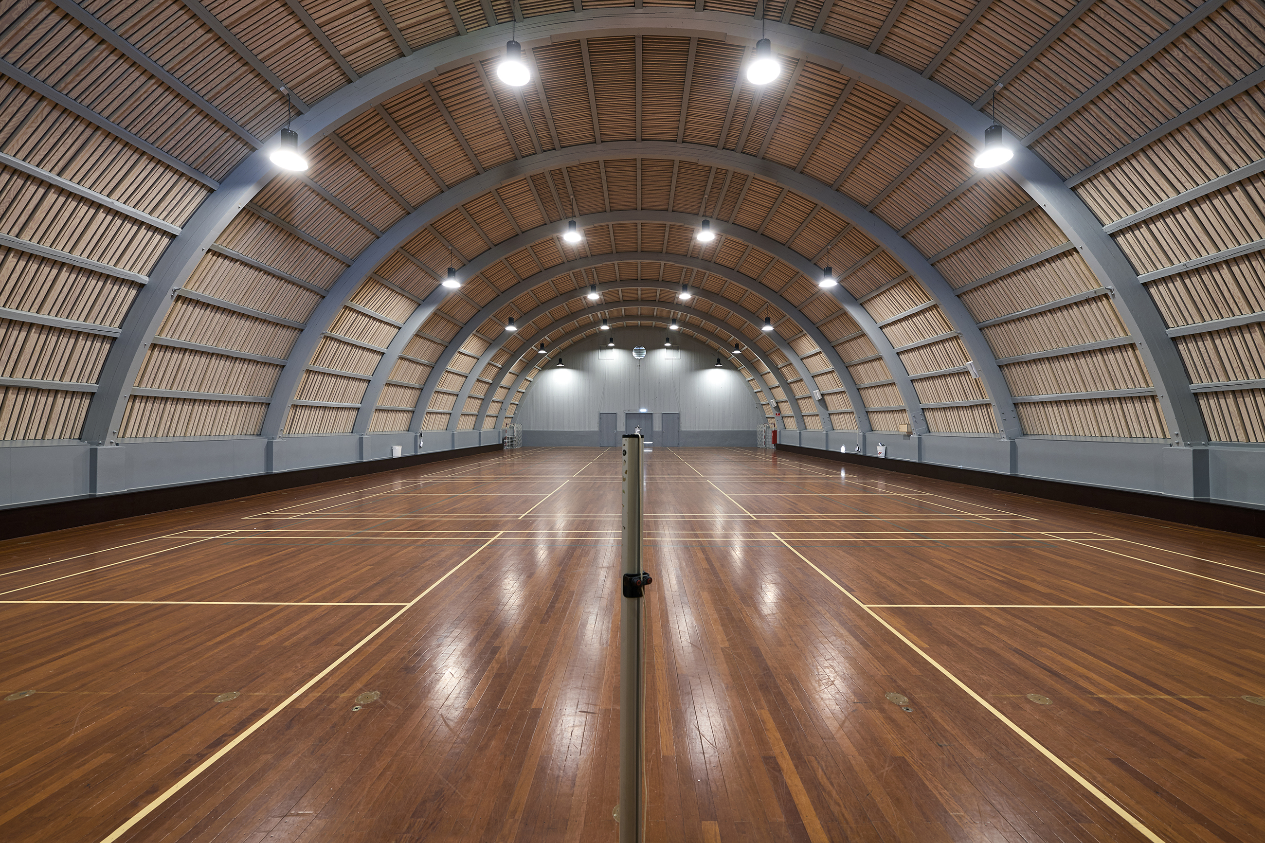 Badmintonhal med mørkt trægulv og rundet loft med trælameller